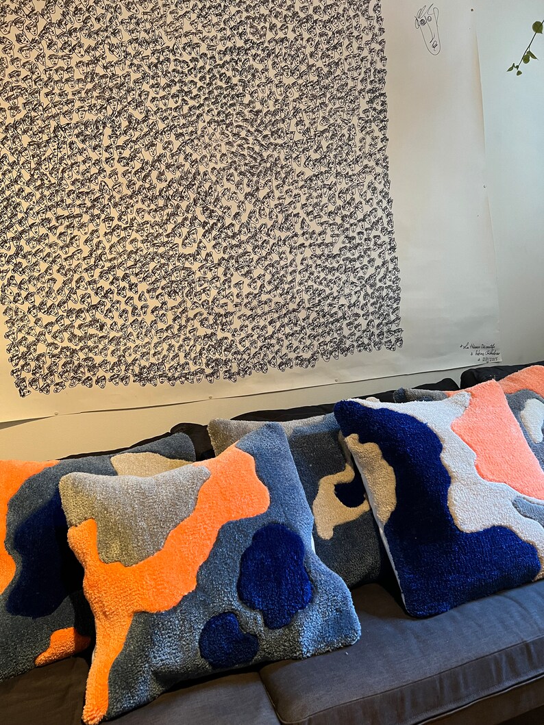 Op de afbeelding: Vier decoratieve kussens met een abstract patroon in blauw, oranje en grijs. De kussens zijn gemaakt van een zachte, pluche stof en hebben een reli&euml;fstructuur.