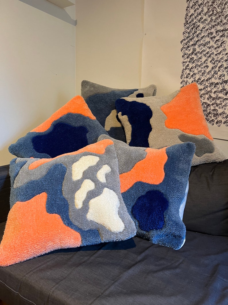 Op de afbeelding: Vijf decoratieve kussens met een kleurrijk abstract patroon in tinten blauw, grijs, wit en oranje. De kussens zijn gemaakt van een zachte, pluche stof en hebben een uniek, modern ontwerp.