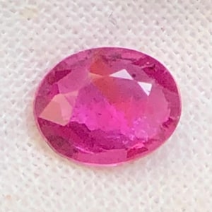 Peut inclure: Une pierre précieuse de taille ovale d'une teinte rose profond avec de multiples facettes qui reflètent la lumière. La pierre présente une surface polie et translucide avec une clarté interne et des bords nets, affichant une couleur magenta saturée.