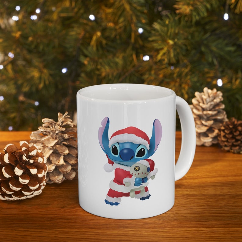 Puede incluir: Taza de cer&aacute;mica blanca con un personaje de dibujos animados azul y rojo que lleva un gorro de Pap&aacute; Noel y sostiene un juguete de peluche. El personaje es Stitch de la pel&iacute;cula de Disney Lilo & Stitch.
