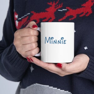 Puede incluir: Taza de cer&aacute;mica blanca con una inscripci&oacute;n azul que dice "MINNIE" en una fuente estilizada.