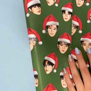 May include: Green wrapping paper with a repeating pattern of a person wearing a red Santa hat. The person's face is visible and the hat is covering their hair.