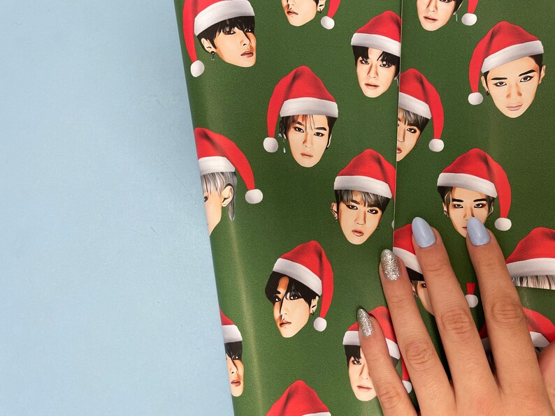 May include: Green wrapping paper with a repeating pattern of a person wearing a red Santa hat. The person's face is visible and the hat is covering their hair.