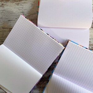 K&ouml;nnte beinhalten: Drei Notizb&uuml;cher mit verschiedenen Papierstilen: leer, gepunktet und liniert. Die Notizb&uuml;cher haben bunte Umschl&auml;ge.