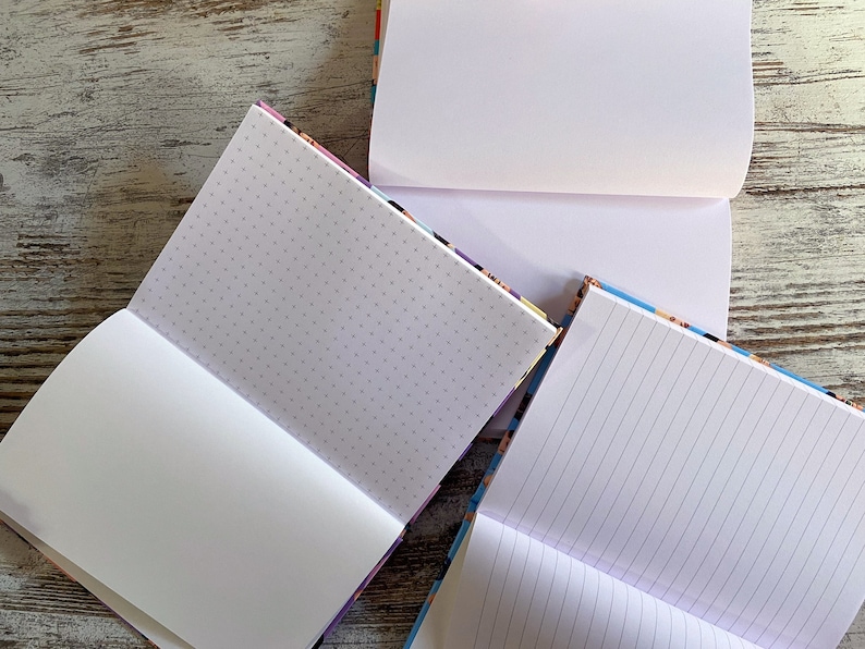 K&ouml;nnte beinhalten: Drei Notizb&uuml;cher mit verschiedenen Papierstilen: leer, gepunktet und liniert. Die Notizb&uuml;cher haben bunte Umschl&auml;ge.