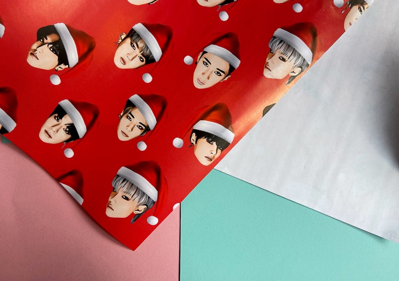 May include: Red wrapping paper with a repeating pattern of a person's face wearing a Santa hat. The person has black hair and is looking directly at the viewer.