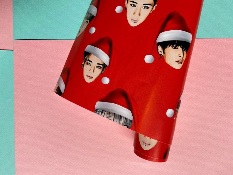 May include: Red wrapping paper with a repeating pattern of men's faces wearing Santa hats. The faces are all different, but they all have the same expression.