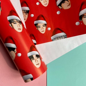 May include: Red wrapping paper with a repeating pattern of Santa hats with faces of people on them.