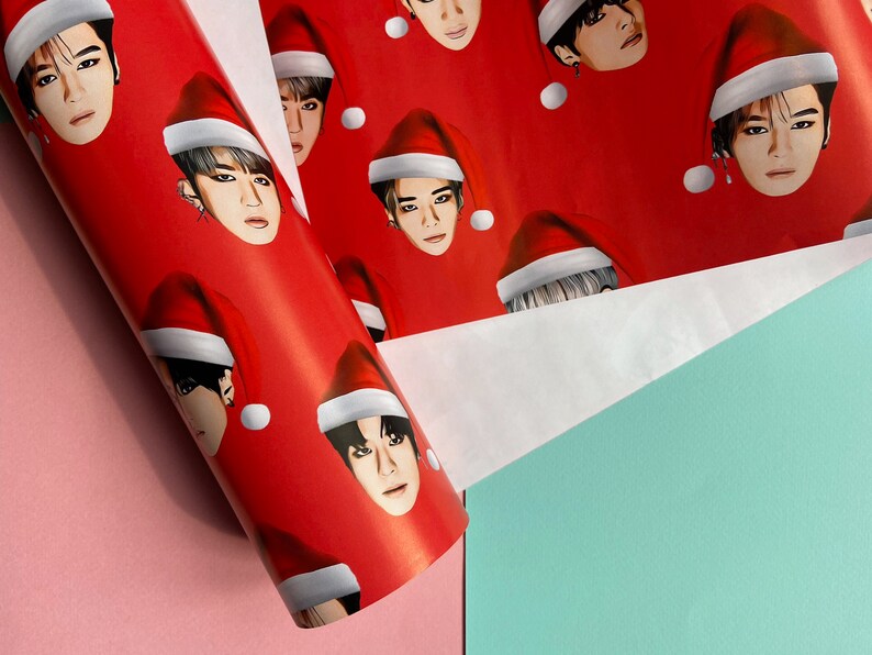 May include: Red wrapping paper with a repeating pattern of Santa hats with faces of people on them.