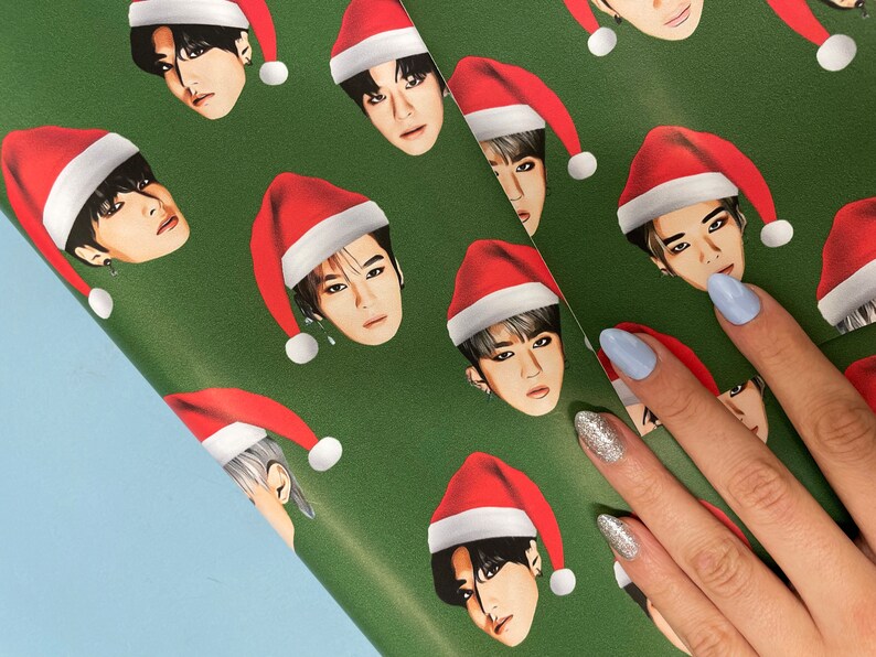 May include: Green wrapping paper with a repeating pattern of cartoon faces wearing Santa hats. The faces are all different, but they all have the same expression.