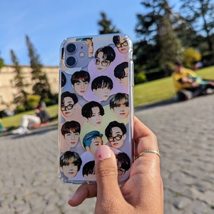 May include: A clear phone case with a colourful pattern of multiple faces of people. The case is being held by a hand with pink nail polish.