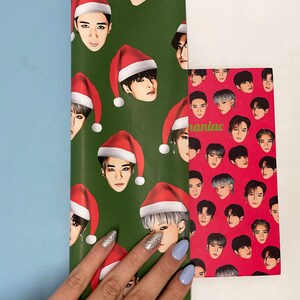 May include: Green and red wrapping paper with a pattern of men wearing Santa hats. The wrapping paper is partially covering a red wrapping paper with a pattern of men's faces. The text "maniac" is visible on the red wrapping paper.