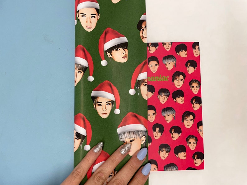 May include: Green and red wrapping paper with a pattern of men wearing Santa hats. The wrapping paper is partially covering a red wrapping paper with a pattern of men's faces. The text "maniac" is visible on the red wrapping paper.