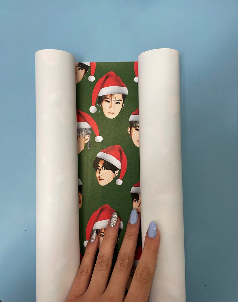 May include: A roll of green wrapping paper with a repeating pattern of a man's face wearing a Santa hat. The paper is partially rolled up and a hand is holding the paper.