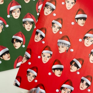 May include: Two sheets of wrapping paper with a repeating pattern of a person wearing a Santa hat. One sheet is red with white dots and the other is green with white dots.