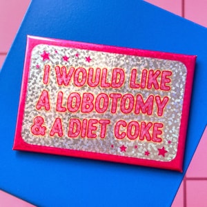 May include: A rectangular, pink-bordered sticker with the text "I WOULD LIKE A LOBOTOMY & A DIET COKE" in pink, glittery letters. The sticker is on a blue surface, set against a pink background.