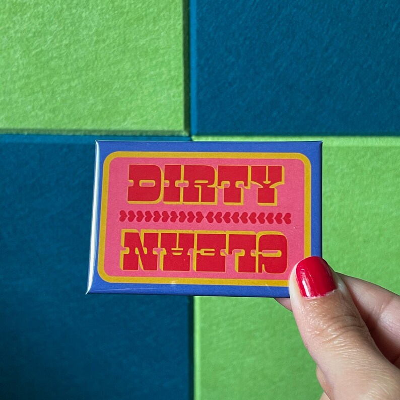 May include: A rectangular magnet with the words "DIRTY" and "CLEAN" in red block letters on a pink background. The magnet is held by a hand with red nail polish.