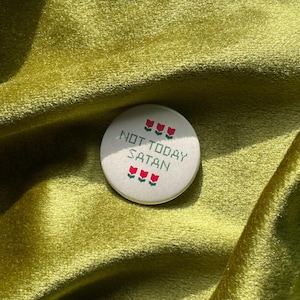 May include: A white button with red embroidered flowers and the text "NOT TODAY SATAN" in green embroidery.