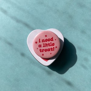 May include: Pink heart-shaped tin with a pink button that says "i need a little treat!" in red letters.