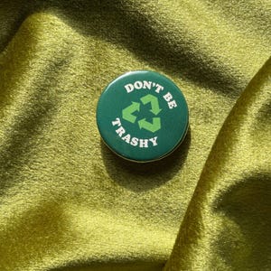 May include: A green button with white text that reads "Don't Be Trashy" and a green recycling symbol.