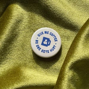 May include: White button with blue text that reads "Give me coffee. No one gets hurt." and a blue coffee cup icon.