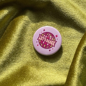 May include: A pink round button with a disco ball graphic and the text "Let's Dance" in a retro font.