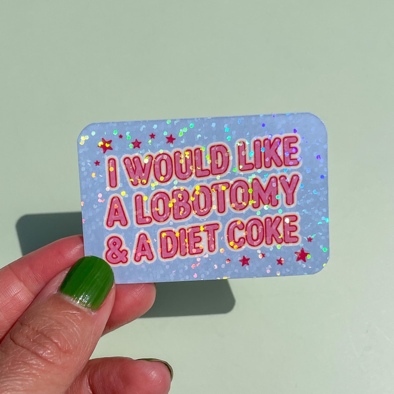 May include: A rectangular sticker with rounded corners, featuring the text "I WOULD LIKE A LOBOTOMY & A DIET COKE" in pink outlined in red. The sticker has a light blue background with glitter and red star accents.