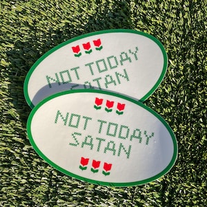Peut inclure: Deux autocollants ovales blancs avec des bordures vertes et des accents de fleurs rouges. Les autocollants disent "Not Today Satan" dans une police de style point de croix.