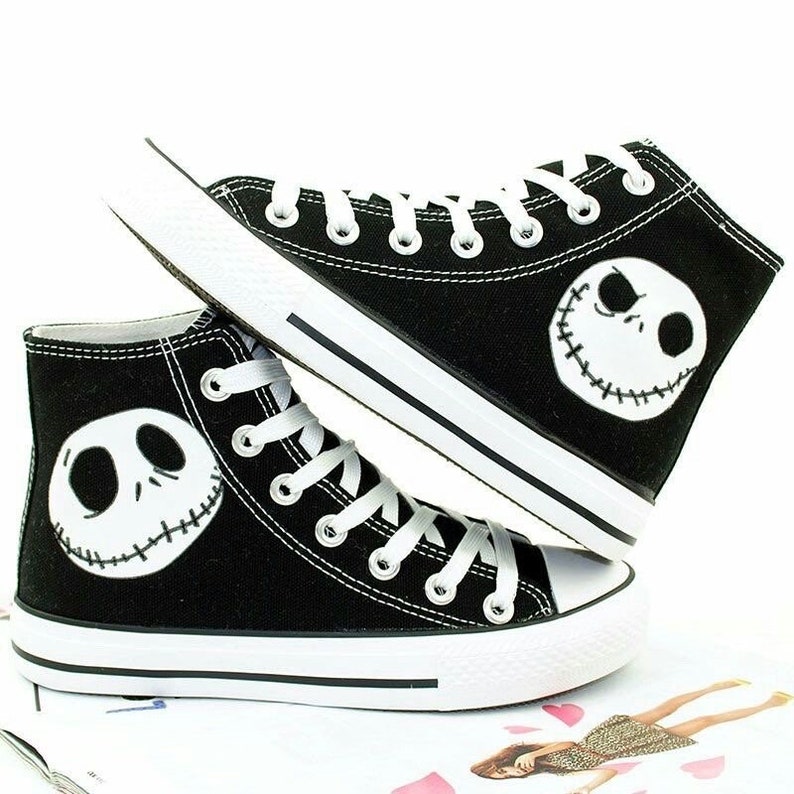 Pu&ograve; includere: Sneakers in tela nera alte con lacci bianchi e suola in gomma bianca. Le scarpe presentano una grafica in bianco e nero del volto di Jack Skellington da The Nightmare Before Christmas.