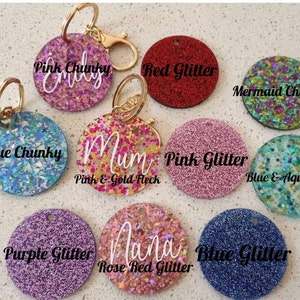 May include: Assortment of round glitter keychains with different colours and text. Keychains include pink chunky glitter with "Emily", blue chunky glitter with "Blue Chunky", pink and gold fleck glitter with "Mum", red glitter with "Red Glitter", pink glitter with "Pink Glitter", blue and aqua fleck glitter with "Blue & Aqua Fleck", purple glitter with "Purple Glitter", rose red glitter with "Nana", and blue glitter with "Blue Glitter".