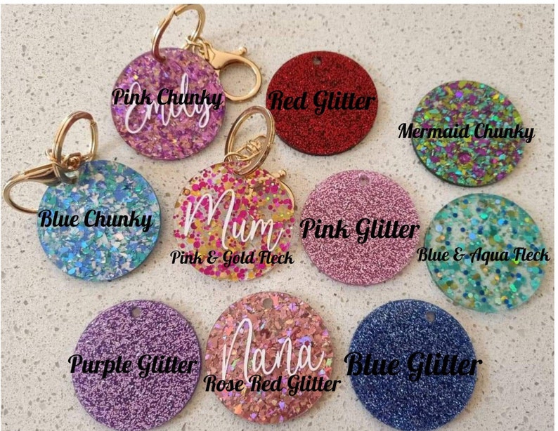 May include: Assortment of round glitter keychains with different colours and text. Keychains include pink chunky glitter with "Emily", blue chunky glitter with "Blue Chunky", pink and gold fleck glitter with "Mum", red glitter with "Red Glitter", pink glitter with "Pink Glitter", blue and aqua fleck glitter with "Blue & Aqua Fleck", purple glitter with "Purple Glitter", rose red glitter with "Nana", and blue glitter with "Blue Glitter".