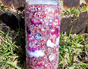 May include: A pink and red glitter tumbler with a Care Bears design. The tumbler features Care Bears with hearts and clouds.
