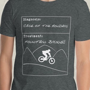 May include: A dark heather grey t-shirt with a white graphic of a medical diagnosis and treatment. The diagnosis is "Case of the Mondays" and the treatment is "Mountain Biking!" with a silhouette of a person riding a mountain bike.