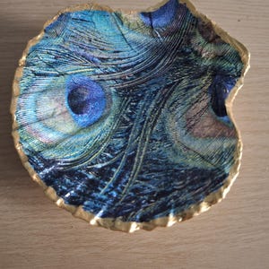 May include: A decorative shell-shaped dish with a peacock feather design. The dish is painted with a blue, green, and gold pattern.