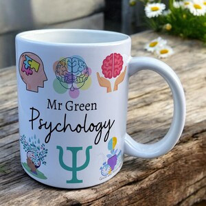 White Ceramic Mug with Psychology Design sat on a table. The Cup has a standard handle. Customisable text is printed below the Psychology design in a black text.