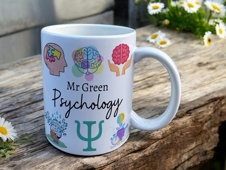 White Ceramic Mug with Psychology Design sat on a table. The Cup has a standard handle. Customisable text is printed below the Psychology design in a black text.