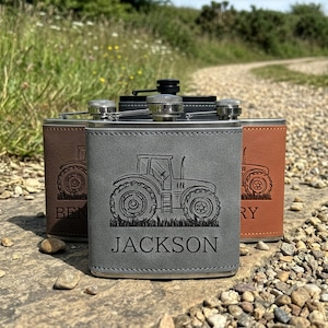 May include: Three rectangular metal flasks wrapped in faux leather in grey, dark brown, and light brown. Each flask features a laser-engraved tractor graphic above a name, with the front grey flask clearly displaying the name JACKSON.