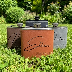 May include: Four rectangular metal flasks wrapped in faux leather in brown, tan, and grey colours. Each flask features a silver screw-top cap and is engraved with a name in script font, along with the text "Officialy Retired" and a date.
