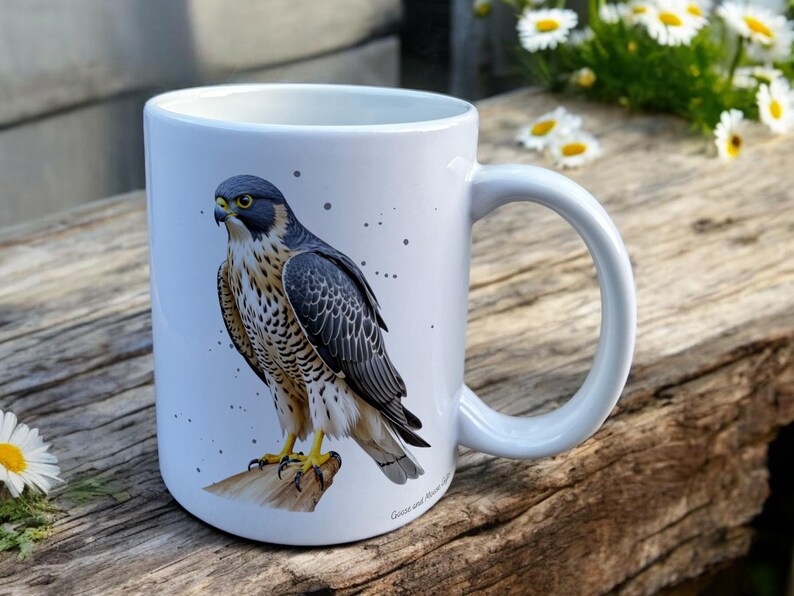 White Ceramic Mug with Falcon Design sat on a table. The Cup has a standard handle. Customisable text is printed below the Falcon design in a black text.