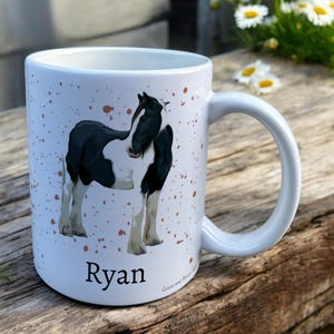 White Ceramic Mug with Horse Design sat on a table. The Cup has a standard handle. Customisable text is printed below the Horse design in a black text.