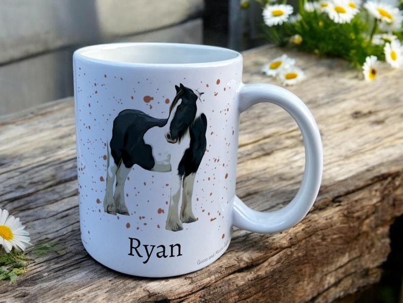 White Ceramic Mug with Horse Design sat on a table. The Cup has a standard handle. Customisable text is printed below the Horse design in a black text.