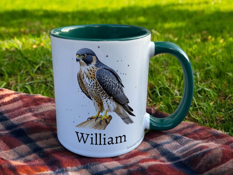 Green & White Ceramic Mug with Falcon Design sat on a table. The Cup has a standard handle. Customisable text is printed below the Falcon design in a black text.