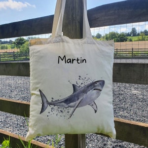 May include: A white canvas tote bag with a black shark illustration and the name "Martin" printed on the front.