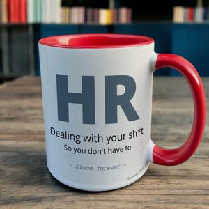 Red & White Ceramic Mug with HR Design sat on a table. The Cup has a standard handle.