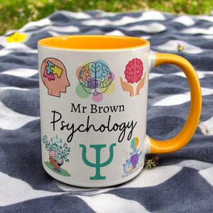 Yellow & White Ceramic Mug with Psychology Design sat on a table. The Cup has a standard handle. Customisable text is printed below the Psychology design in a black text.
