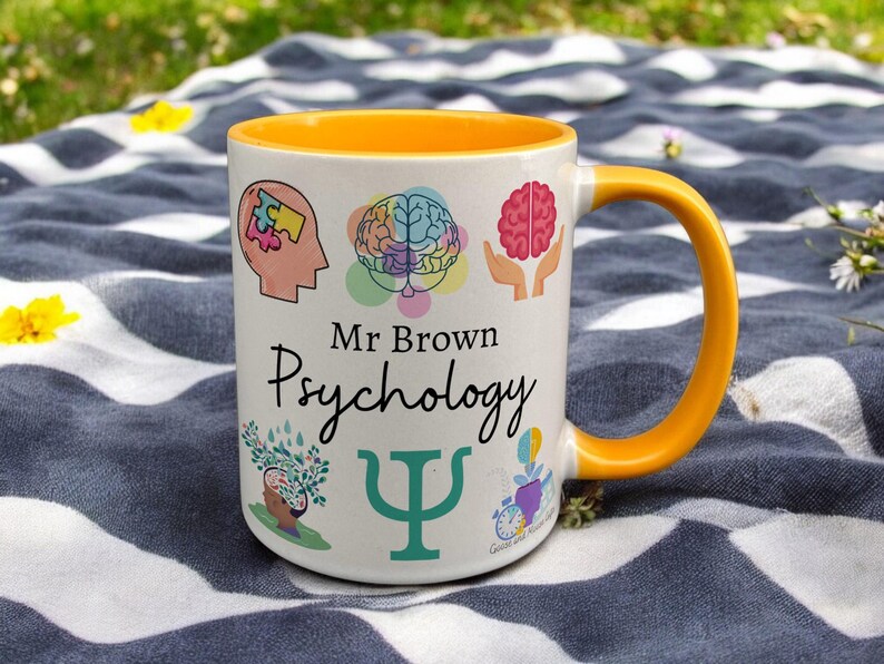 Yellow & White Ceramic Mug with Psychology Design sat on a table. The Cup has a standard handle. Customisable text is printed below the Psychology design in a black text.