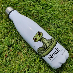 May include: A light blue stainless steel water bottle with a green snake graphic and the name "Noah" printed on the side. The bottle is on a bed of green grass.