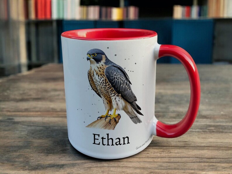 Red & White Ceramic Mug with Falcon Design sat on a table. The Cup has a standard handle. Customisable text is printed below the Falcon design in a black text.