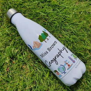 May include: White insulated water bottle with a blue, green, and brown design featuring a mountain, trees, a globe, a lighthouse, and a thermometer. The text "Miss Brown Geography" is printed on the bottle.