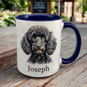 May include: White ceramic mug with a dark blue interior and handle. The mug features a watercolor-style portrait of a black poodle with the name "Joseph" printed below. The mug has a glossy finish.
